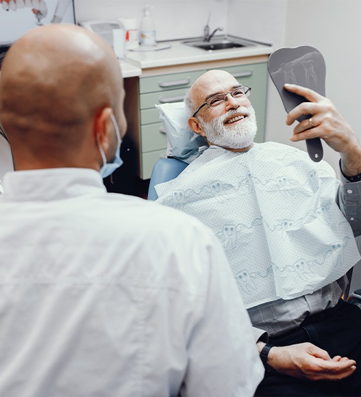 Man looking at smile in mirror after dental implant tooth replacement