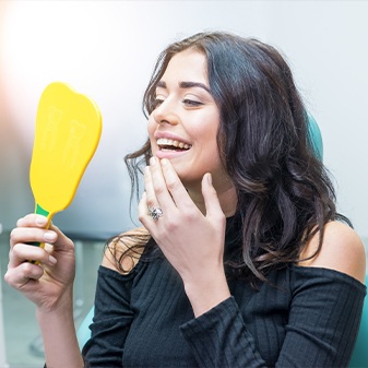 Woman examining her dental implant supported dental restoration in mirror