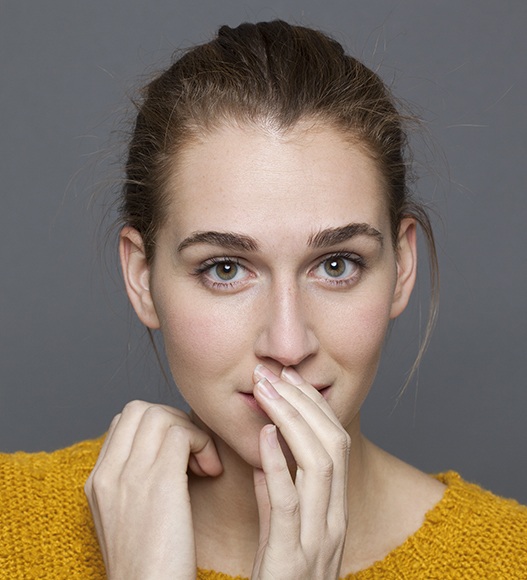 Woman in need of dental bonding covering her mouth