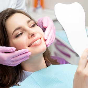 Happy dental patient using mirror to admire the results of her cosmetic treatment