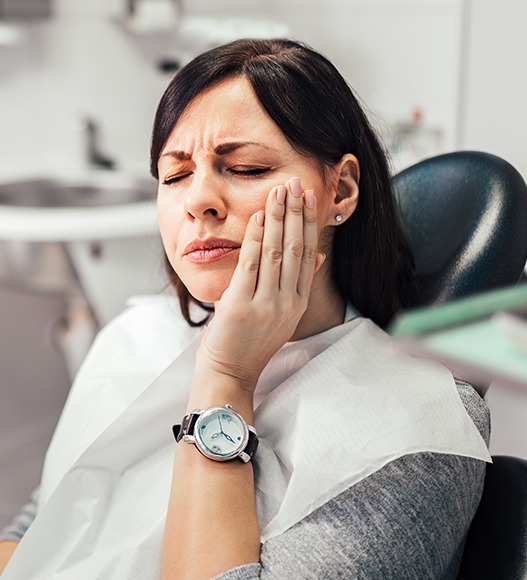 Woman at dentist for emergency dentistry holding cheek in pain