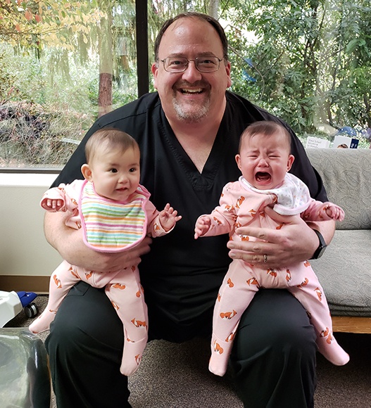 Dentist holding two infants after dental checkup and teeth cleanings for kids