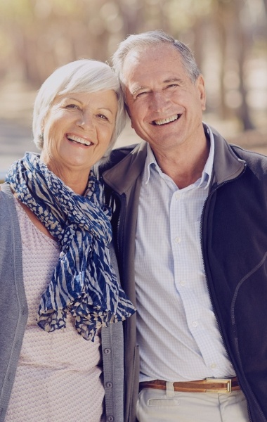 Older man and woman smiling after replacing missing teeth