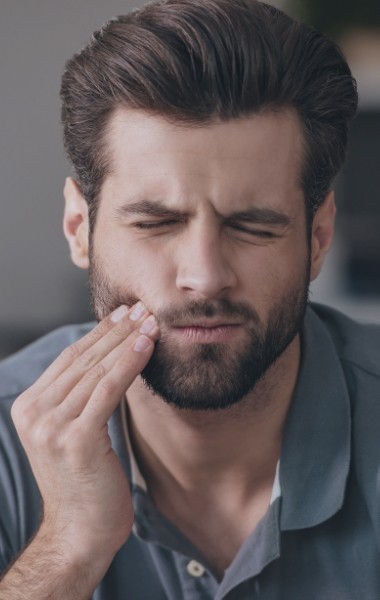 Man in need of emergency dentistry holding cheek in pain