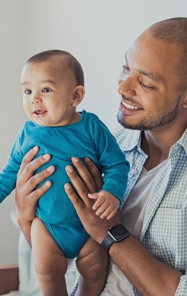 Father holding smiling infant after lip and tongue tie treatment