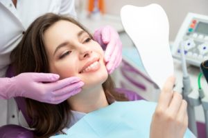 Patient visiting cosmetic dentist, holding mirror while relaxing