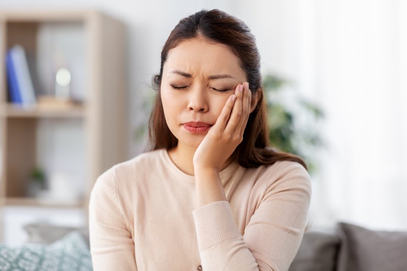 A woman holding her cheek while suffering a toothache